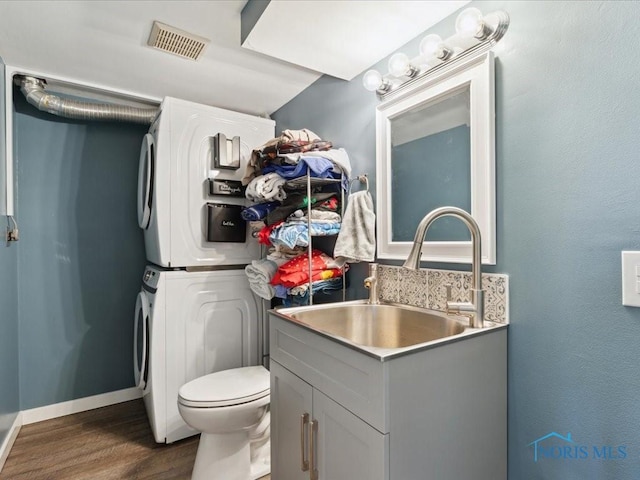 bathroom featuring stacked washing maching and dryer, hardwood / wood-style floors, vanity, and toilet