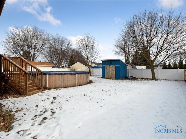 yard covered in snow featuring a swimming pool side deck and a storage unit