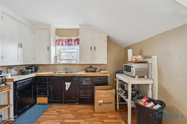 kitchen featuring tasteful backsplash, lofted ceiling, sink, white cabinets, and light hardwood / wood-style flooring