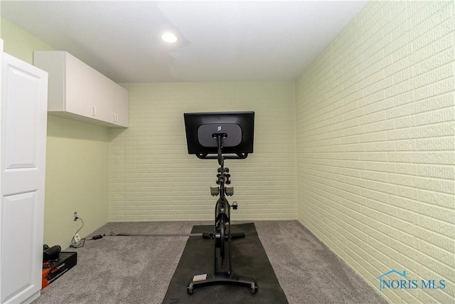 exercise room featuring brick wall and dark colored carpet