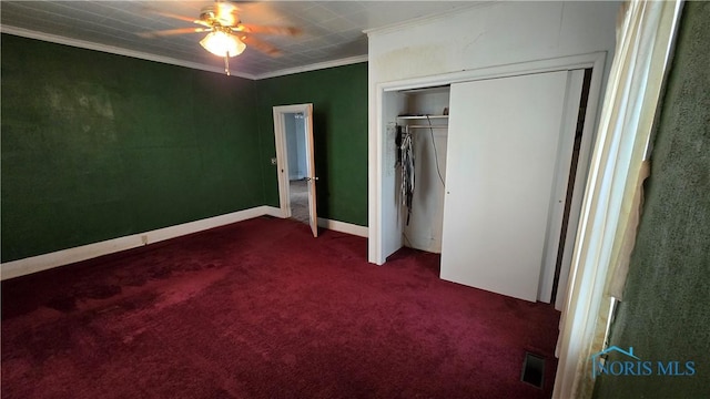 unfurnished bedroom with ornamental molding, dark carpet, ceiling fan, and a closet