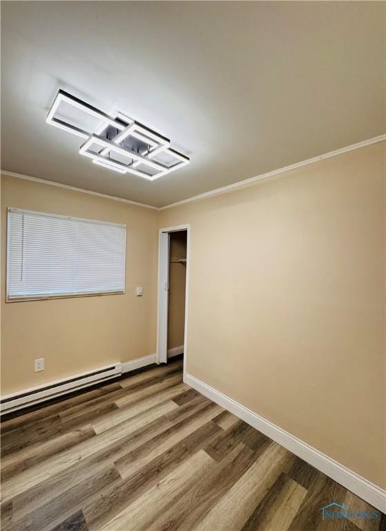 spare room with crown molding, wood-type flooring, and a baseboard heating unit