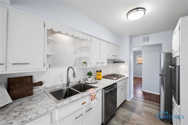 kitchen with sink, appliances with stainless steel finishes, white cabinetry, wood-type flooring, and light stone countertops