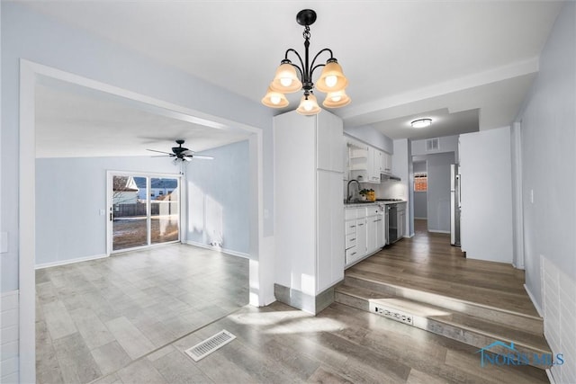 kitchen with ceiling fan with notable chandelier, stainless steel refrigerator, decorative light fixtures, sink, and white cabinets