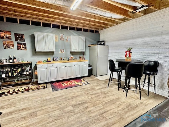 bar with brick wall, white cabinetry, wooden counters, white fridge, and light wood-type flooring