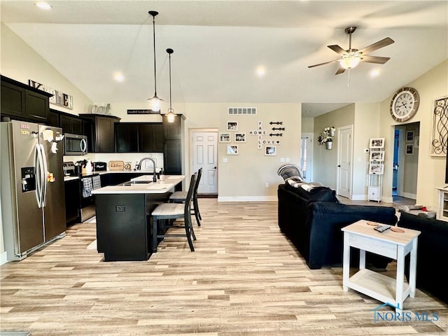 kitchen featuring sink, a breakfast bar, appliances with stainless steel finishes, hanging light fixtures, and a center island with sink