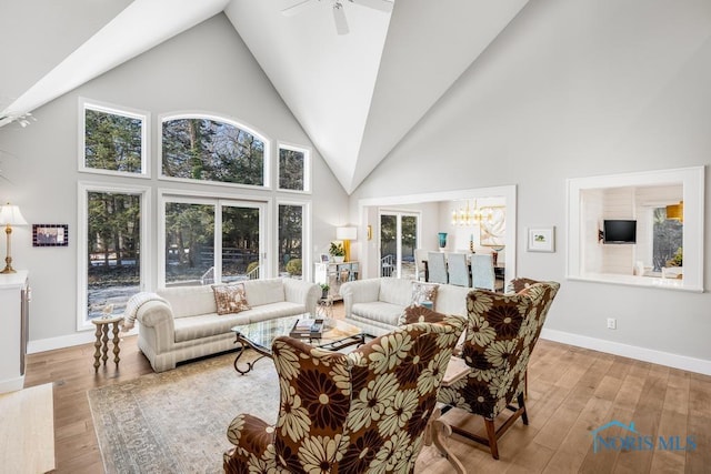 living room with ceiling fan with notable chandelier, high vaulted ceiling, and light hardwood / wood-style flooring