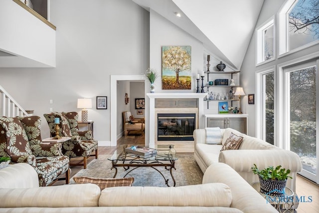 living room with light hardwood / wood-style flooring, a wealth of natural light, high vaulted ceiling, and a premium fireplace