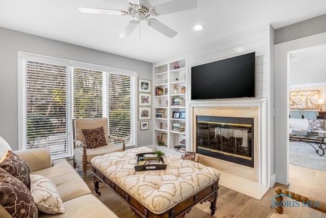 living room featuring built in features, a high end fireplace, light hardwood / wood-style floors, and ceiling fan