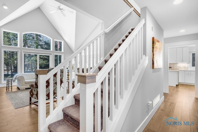 stairway featuring hardwood / wood-style flooring, ceiling fan, and high vaulted ceiling