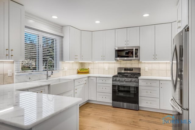 kitchen featuring tasteful backsplash, sink, white cabinets, stainless steel appliances, and light wood-type flooring