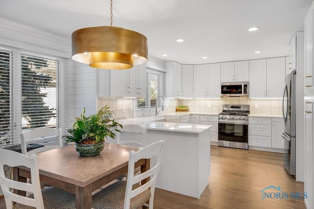 kitchen with decorative light fixtures, appliances with stainless steel finishes, kitchen peninsula, decorative backsplash, and white cabinets