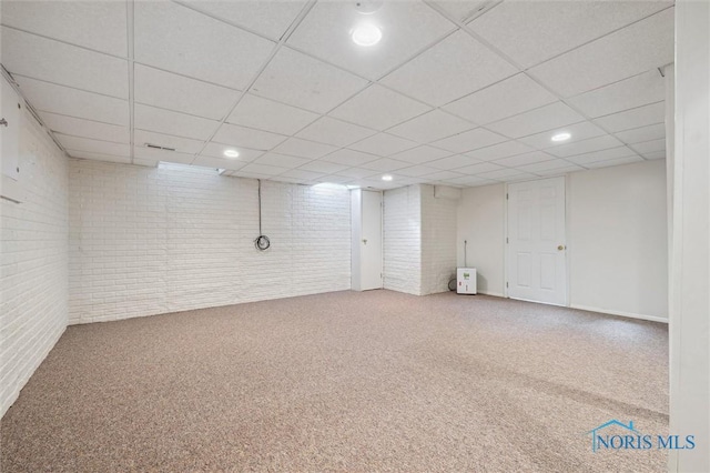 basement with brick wall, carpet, and a paneled ceiling