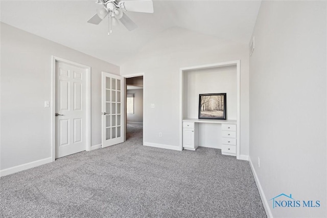 unfurnished bedroom featuring lofted ceiling, carpet floors, built in desk, and ceiling fan