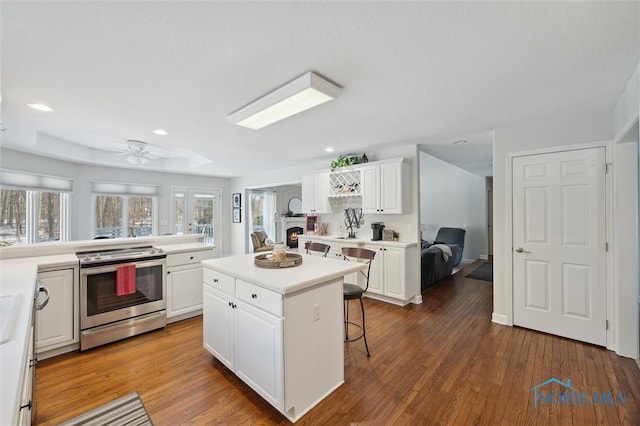 kitchen with a breakfast bar, white cabinetry, a kitchen island, electric stove, and hardwood / wood-style floors