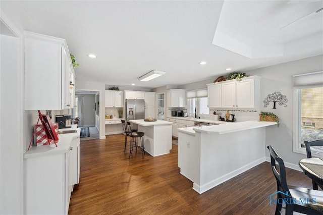 kitchen featuring a kitchen island, appliances with stainless steel finishes, white cabinets, a kitchen breakfast bar, and kitchen peninsula