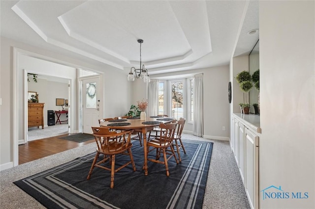 carpeted dining room featuring an inviting chandelier and a tray ceiling