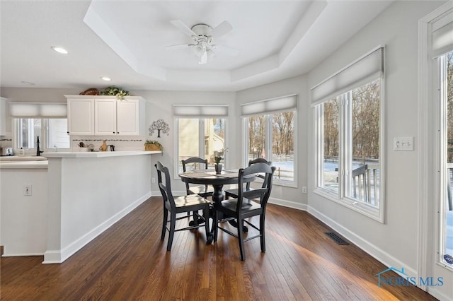 dining area with dark hardwood / wood-style floors, ceiling fan, and a tray ceiling