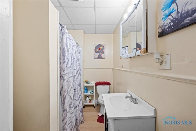 bathroom with toilet, a paneled ceiling, wood-type flooring, vanity, and curtained shower