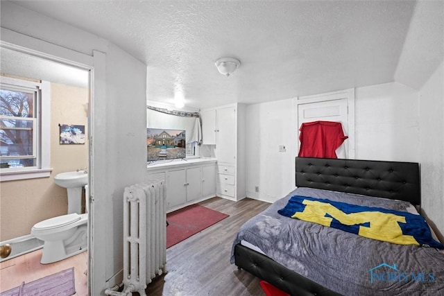 bedroom with vaulted ceiling, radiator heating unit, hardwood / wood-style floors, and a textured ceiling