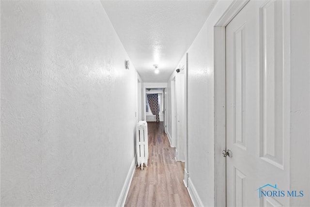 hallway featuring radiator heating unit, hardwood / wood-style floors, and a textured ceiling