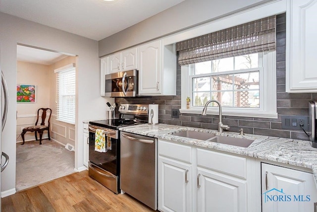 kitchen with white cabinetry, sink, backsplash, light hardwood / wood-style floors, and stainless steel appliances