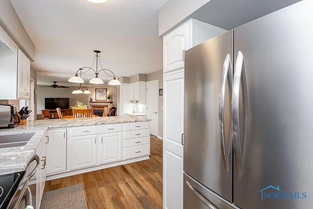 kitchen with stainless steel appliances, white cabinetry, light stone countertops, and decorative light fixtures