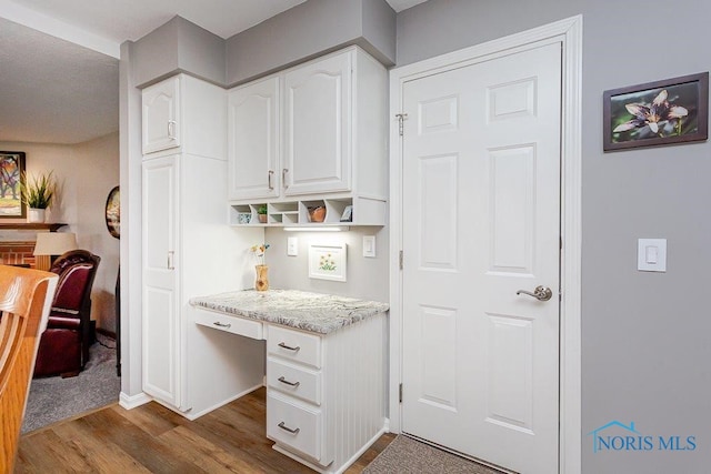 kitchen with light stone counters, hardwood / wood-style flooring, built in desk, and white cabinets