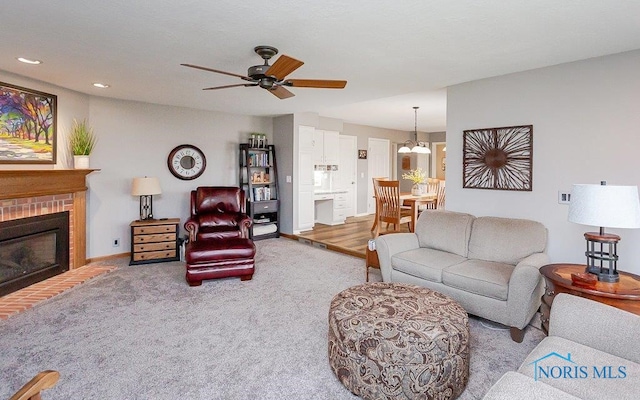 carpeted living room with ceiling fan with notable chandelier and a brick fireplace