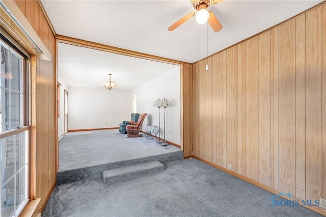 empty room with ceiling fan with notable chandelier, wooden walls, and carpet floors