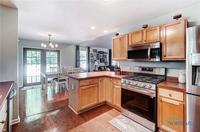 kitchen featuring appliances with stainless steel finishes, decorative light fixtures, kitchen peninsula, a chandelier, and light wood-type flooring