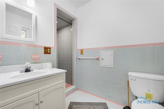 bathroom with tile walls, vanity, toilet, and a tile shower