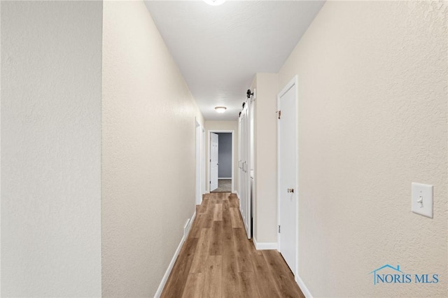 corridor with a barn door and light hardwood / wood-style flooring