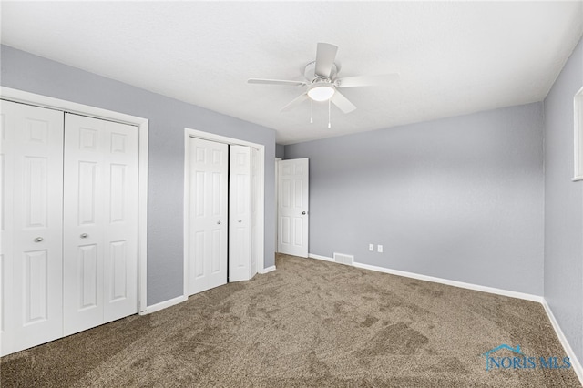 unfurnished bedroom featuring ceiling fan, carpet flooring, and two closets