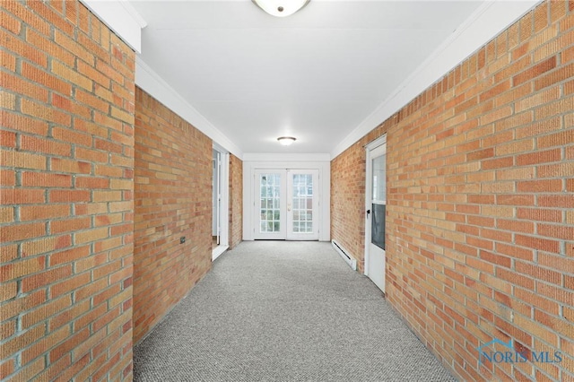 hallway with crown molding, a baseboard heating unit, carpet flooring, brick wall, and french doors