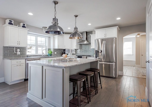 kitchen with white cabinetry, stainless steel fridge, wall chimney exhaust hood, and a kitchen island