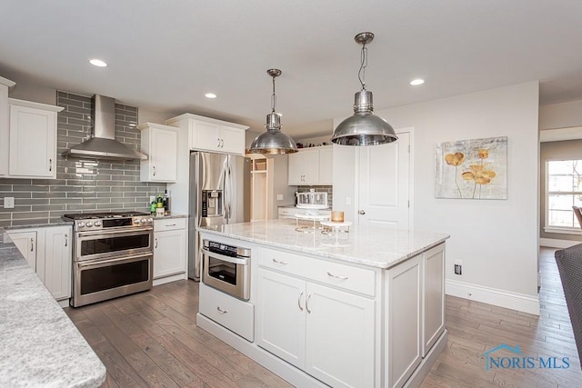 kitchen with wall chimney exhaust hood, tasteful backsplash, light stone counters, appliances with stainless steel finishes, and white cabinets