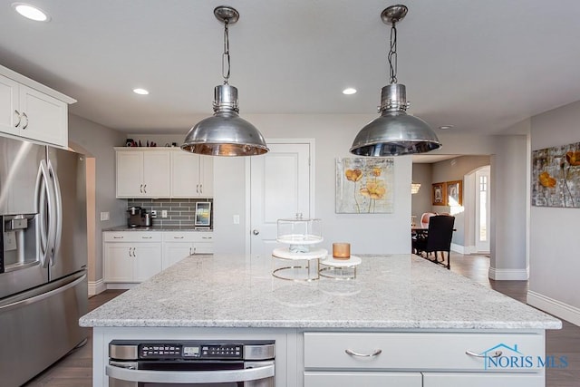 kitchen featuring stainless steel fridge, a kitchen island, white cabinets, light stone countertops, and backsplash