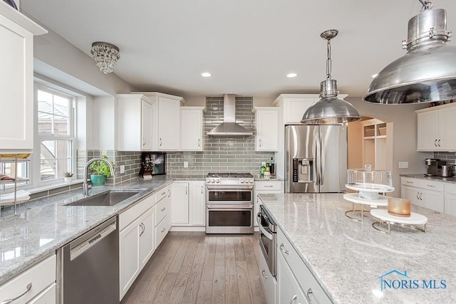 kitchen featuring white cabinetry, wall chimney range hood, sink, and appliances with stainless steel finishes