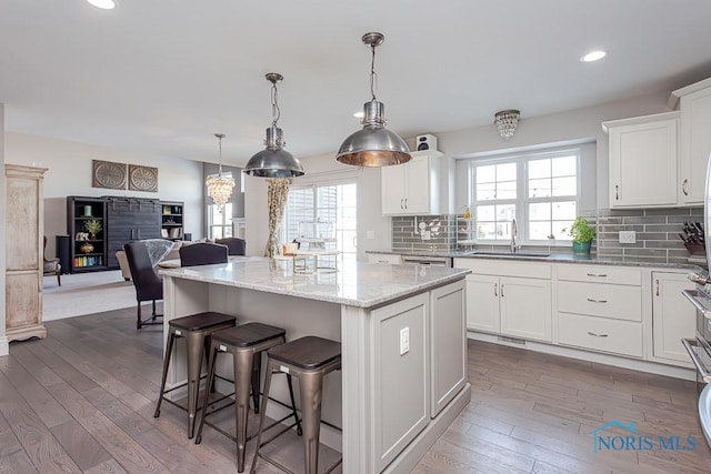 kitchen featuring pendant lighting, sink, white cabinetry, backsplash, and a center island