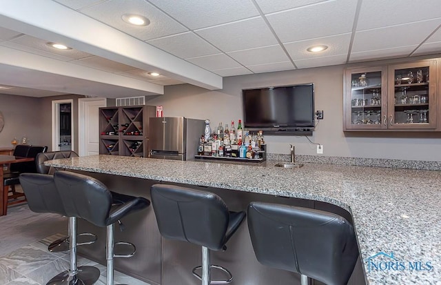 bar with sink, stainless steel fridge, a paneled ceiling, beam ceiling, and light stone counters