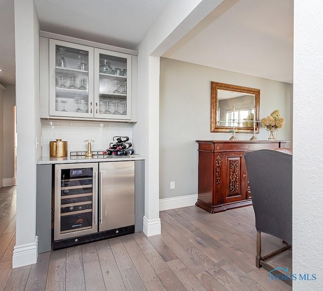 bar with decorative backsplash, beverage cooler, and hardwood / wood-style flooring