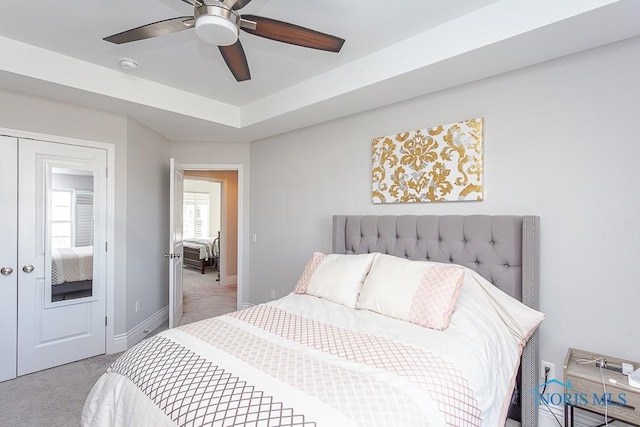 carpeted bedroom with ceiling fan, a raised ceiling, and a closet