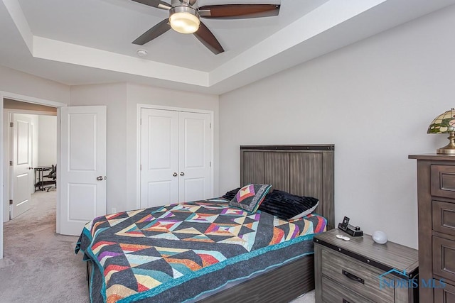 carpeted bedroom featuring a tray ceiling, a closet, and ceiling fan