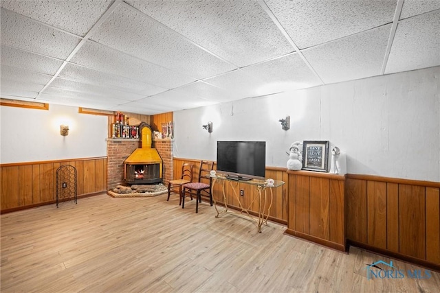 sitting room featuring a drop ceiling, light wood-type flooring, wood walls, and a wood stove