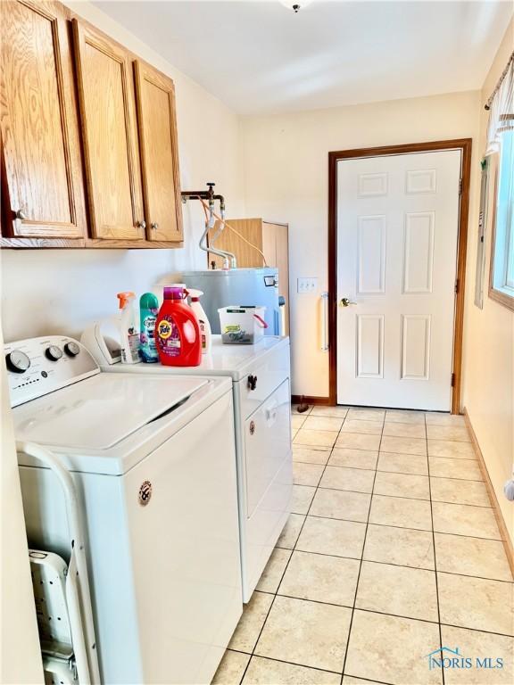 clothes washing area featuring cabinets, washing machine and clothes dryer, water heater, and light tile patterned floors