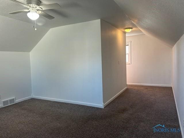 additional living space featuring ceiling fan, lofted ceiling, a textured ceiling, and dark colored carpet