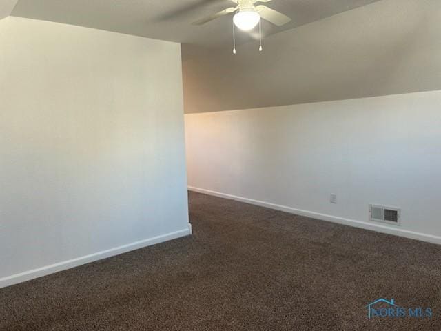 spare room featuring lofted ceiling, dark carpet, and ceiling fan