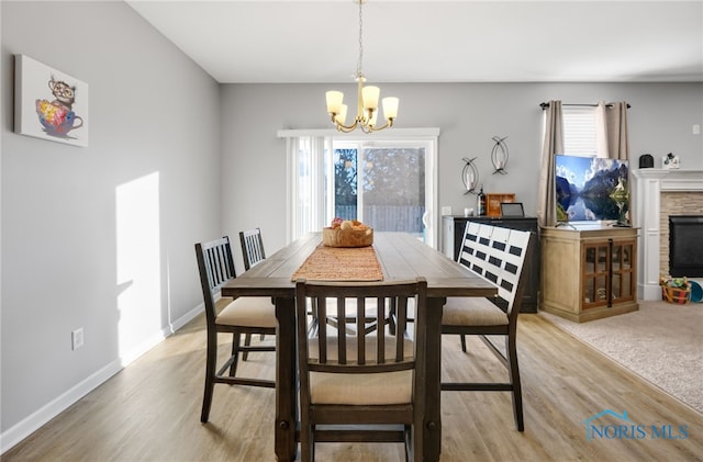 dining space with an inviting chandelier, a fireplace, and light hardwood / wood-style floors