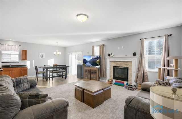 living room with plenty of natural light, a stone fireplace, and a notable chandelier